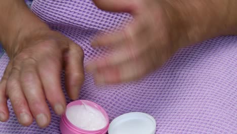 old lady apply white moisturizer cream on her wrinkled skin hand. senior women skincare