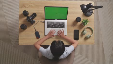 top view of a woman video editor using green screen laptop and smartphone next to the camera in the workspace at home