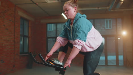 healthy caucasian woman exercising workout on stationary cycling machine bike in gym, slow motion