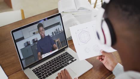 African-american-male-college-student-holding-notes-while-having-a-video-call-on-laptop-at-home