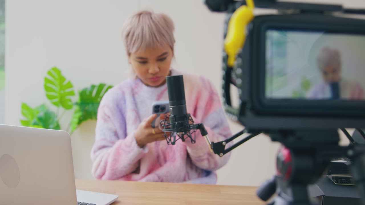 Inquadratura dalla fotocamera di una vlogger che guarda il telefono cellulare prima di una diretta streaming