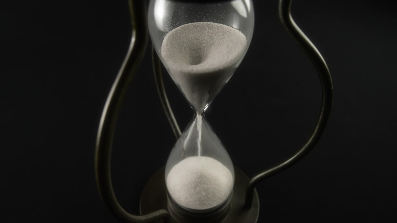 Hourglass Measuring Time with White Sand Flowing on Black Background