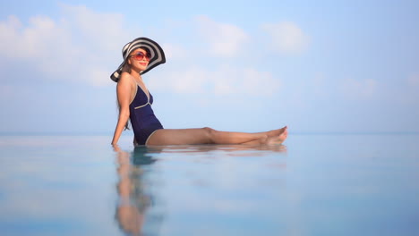 Perfil-De-Una-Mujer-Joven-Sana-Sentada-Al-Borde-De-Una-Piscina-Infinita-Contra-Un-Horizonte-Azul-Del-Océano