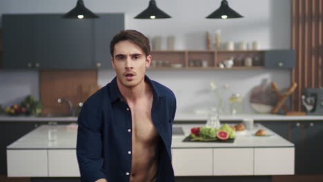 Attractive-guy-dancing-at-home-kitchen.-Sexy-man-in-open-skirt-looking-to-camera