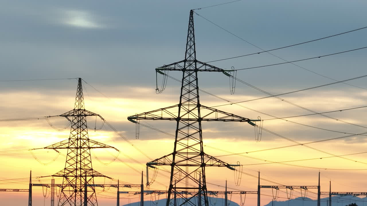 Power lines and electrical transmission towers stand tall in the rural area as the sun sets behind