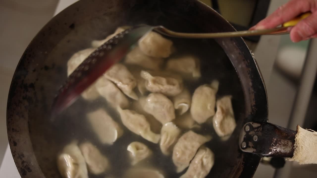 Chef slowly stirs a wok of boiling dumpings