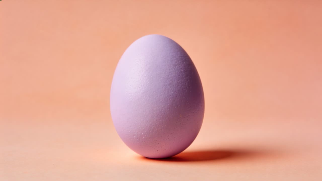 Wobbling pastel lavender egg toppling, rolling right on peach table casting soft shadow