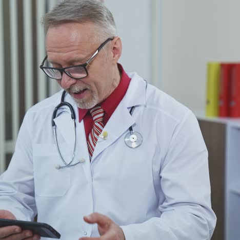 senior doctor with a phone in medical center. grey haired therapist in medical white coat with stethoscope giving consultation through the mobile phone in clinic.