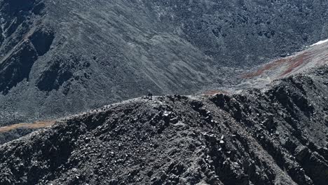 drone orbits above friends at summit of a rugged dirt trail on peak 10 in breckenridge, colorado, leading through rocky talus terrain, telephoto depth