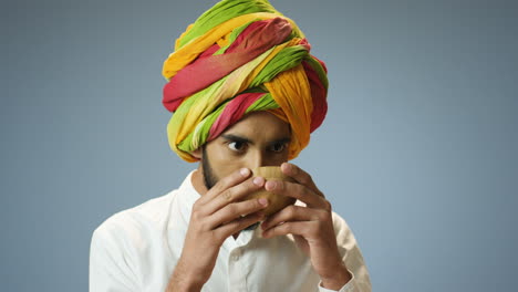 close-up view of young cheerful indian man in traditional clothes and turban drinking tea from a cup