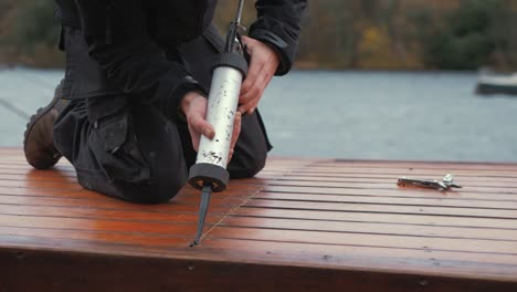 young man seals roof planking of wooden boat with sika flex gun