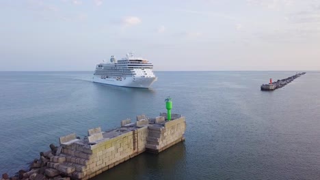 Aerial-view-of-large-white-cruise-liner-Seven-Seas-Splendor-arriving-at-the-port-of-Liepaja-,-early-morning-golden-hour,-water-transportation,-Baltic-sea,-vacation,-wide-shot-moving-forward