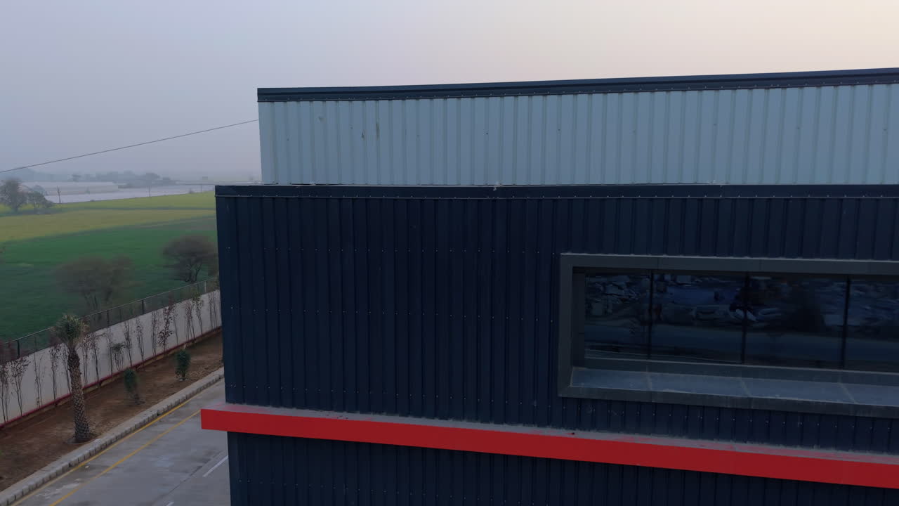 Una prospettiva aerea che mostra un moderno magazzino industriale e uno stabilimento di produzione ingegneristica accanto a campi verdi all'alba.
