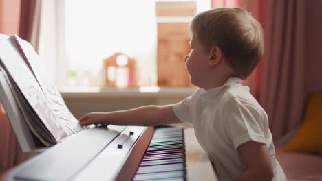 Smart-boy-turns-music-sheets-sitting-at-electrical-piano