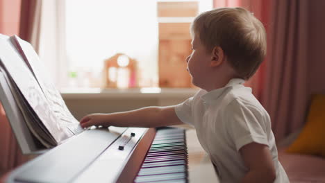 smart boy turns music sheets sitting at electrical piano