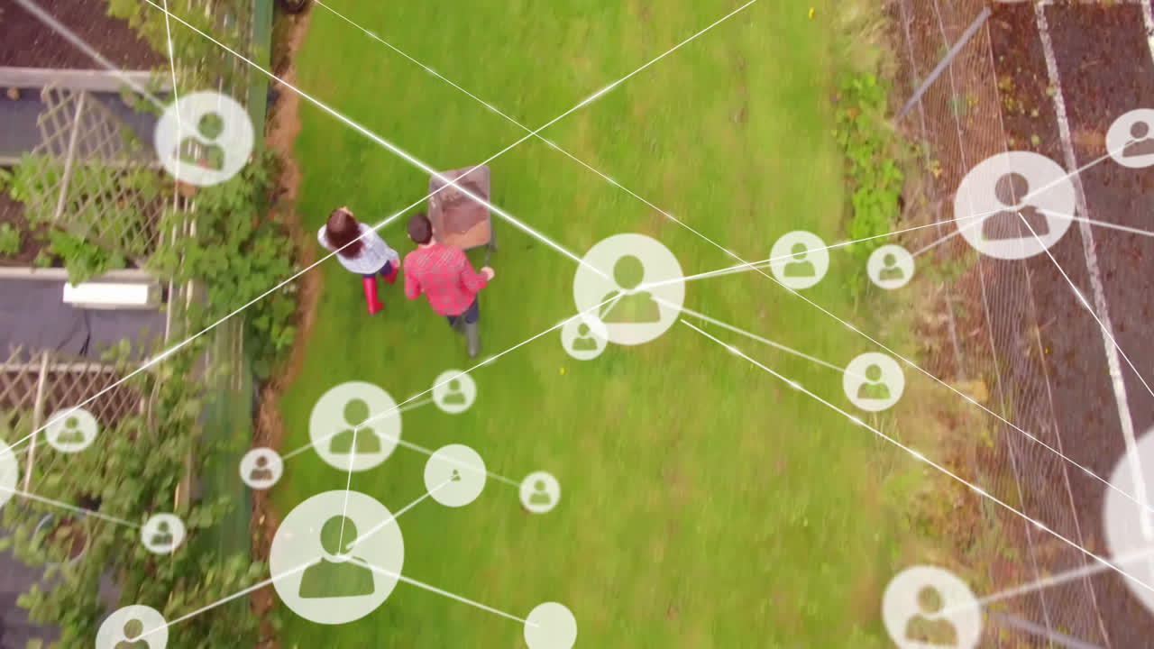 red de iconos de perfil contra vista aérea de pareja caucásica con carrito de jardín en el jardín