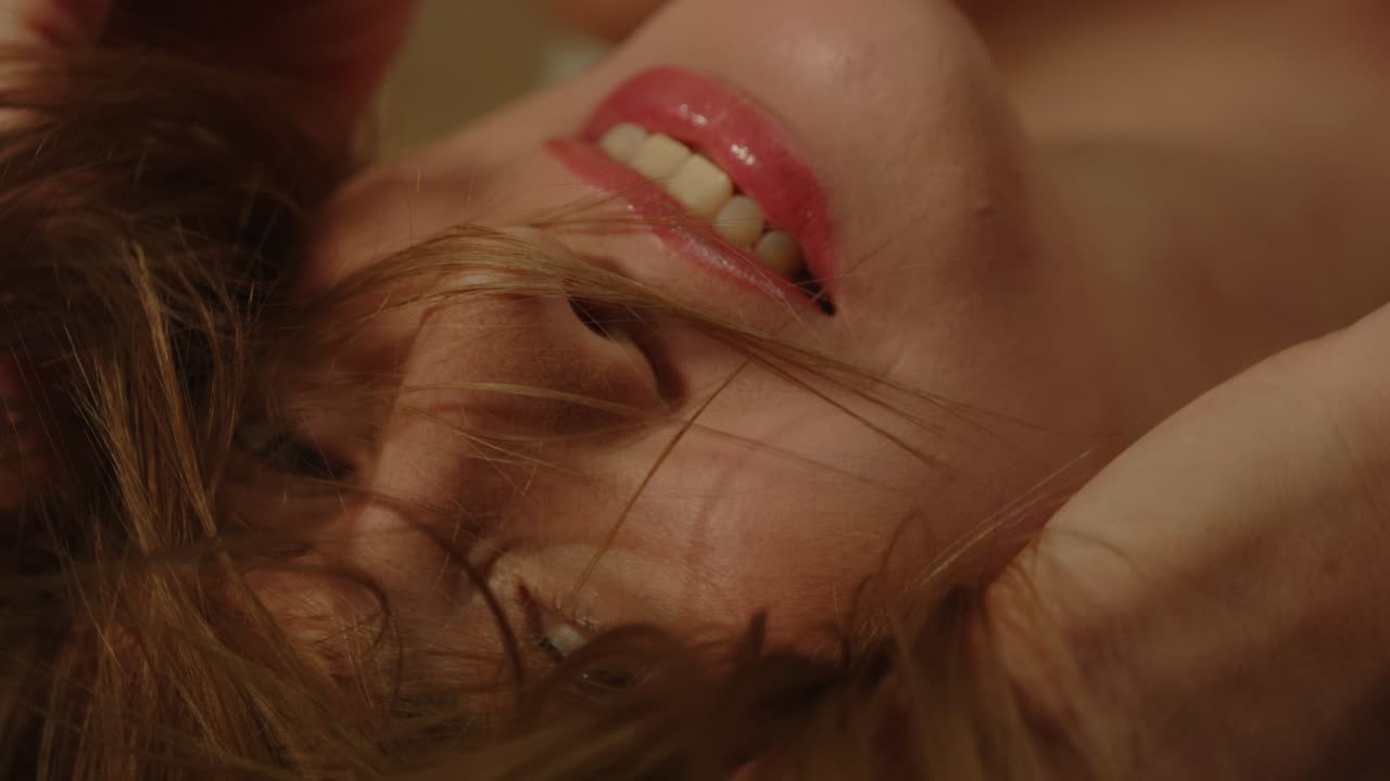 beautiful macro of an attractive joyful woman smiling and sensually playing with her hair in slow motion
