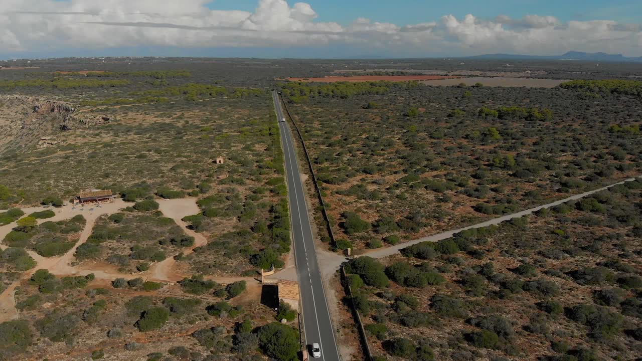 모래, 돌, 덤불로 뒤덮인 평평한 풍경 속에서 도로 위를 날아다니는 드론 영상, 그 위를 달리는 자동차