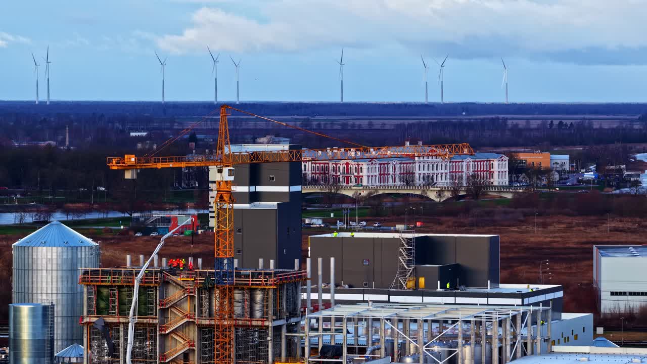 Gru industriali vicino a un edificio storico, turbine eoliche sullo sfondo