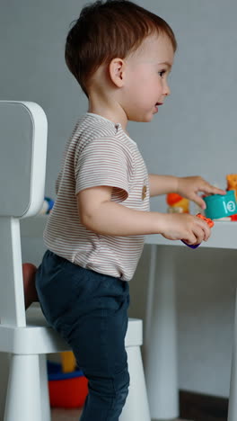 beautiful toddler plays with his toys at the little white desk. child takes a toy tiger and looks at it. vertical video