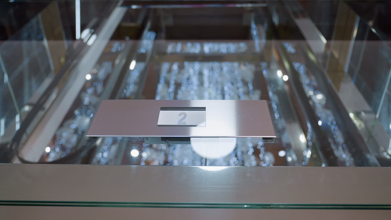 Close up of modern elevator floor indicator showing number two as elevator descends, reflections of festive lights on glass inside shopping mall interior