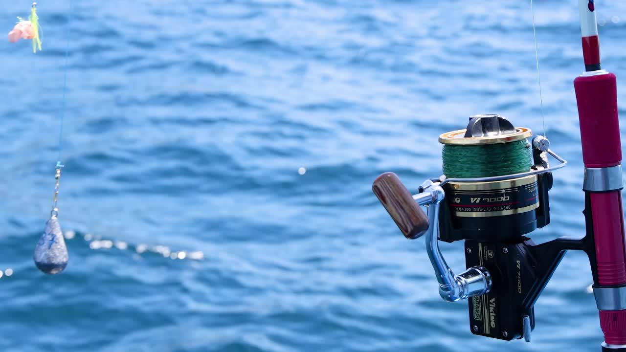 Close-up of a fishing reel and line with weights, set against a backdrop of ocean waves.