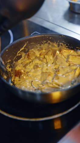 preparing the potatoes in the cheese sauce. cook stirs the dish in frying pan. close up. blurred backdrop. vertical video.