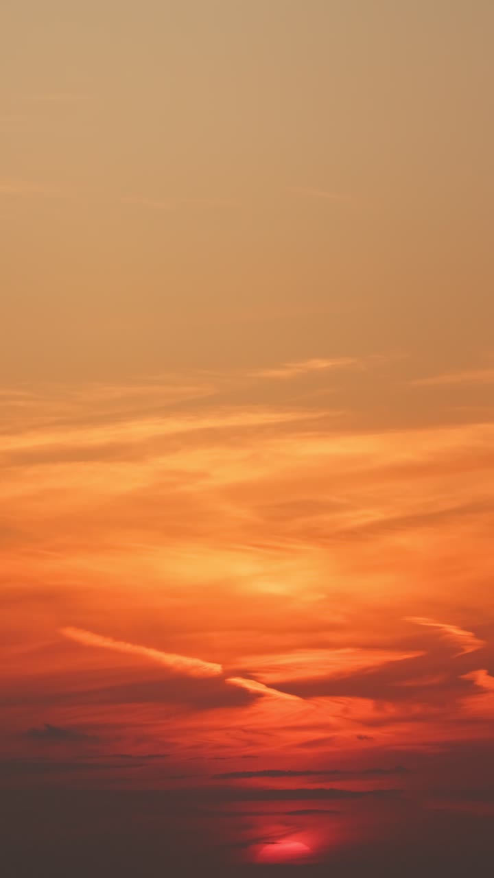 Slow vertical shot of a vivid sunset descending over a calm sea