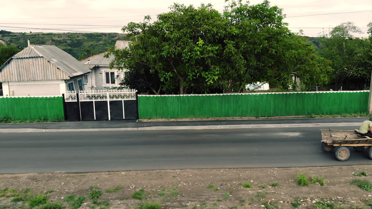 Orhei, Moldova - September 10, 2021: A traditional rural scene featuring a man riding a wooden horse drawn cart along a quiet road lined with old houses and trees