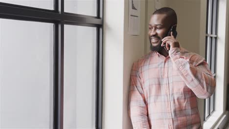 happy african american casual businessman talking on smartphone in office, copy space, slow motion