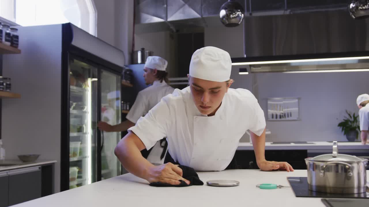 un chef masculino caucásico profesional que lleva limpiando una encimera, con colegas trabajando