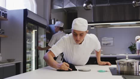 a professional caucasian male chef wearing cleaning a counter top, with colleagues working