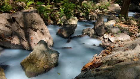 sulphuric stream with white, milky hot water flowing through a rocky river in remote forest in timor leste, southeast asia