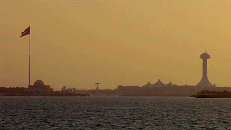 la bandera de los emiratos árabes unidos ondea en el viento contra la silueta de abu dhabi
