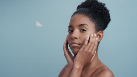 slow motion portrait beautiful african american woman feathers falling on smooth skin touching bare shoulders enjoying natural skincare beauty gently caressing body in blue background