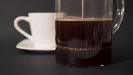 Making-coffee-in-french-press---closeup-of-pressing-plunger-down,-white-cup-in-the-background