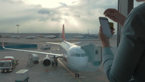 In-airport-view-of-woman-making-payment-with-bank-card-using-smartphone-and-dongle-for-scanning-bank-card