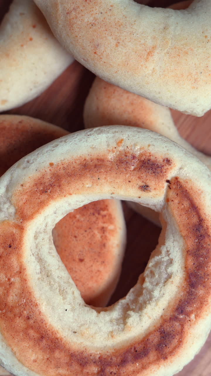 This vertical video showcases a close-up shot of freshly baked pandebono, emphasizing the golden crust and soft texture in warm, inviting lighting. Ideal for food lovers and social media