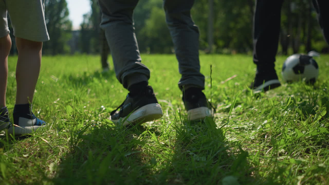 잔디에 서있는 개인의 근접 다리 뷰, 그들 가운데 축구 공을 가지고 야외 운동에 종사하고, 배경에는 골 포스트의 흐릿한 시야가 있습니다.