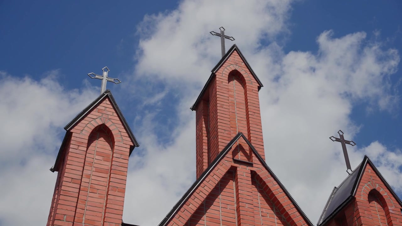 Inquadratura ravvicinata che sale lungo la facciata di una chiesa in mattoni rossi e le torri sormontate da croci, in pieno giorno. La messa a fuoco nitida evidenzia gli archi gotici e la lavorazione dettagliata. Nessuno visibile.