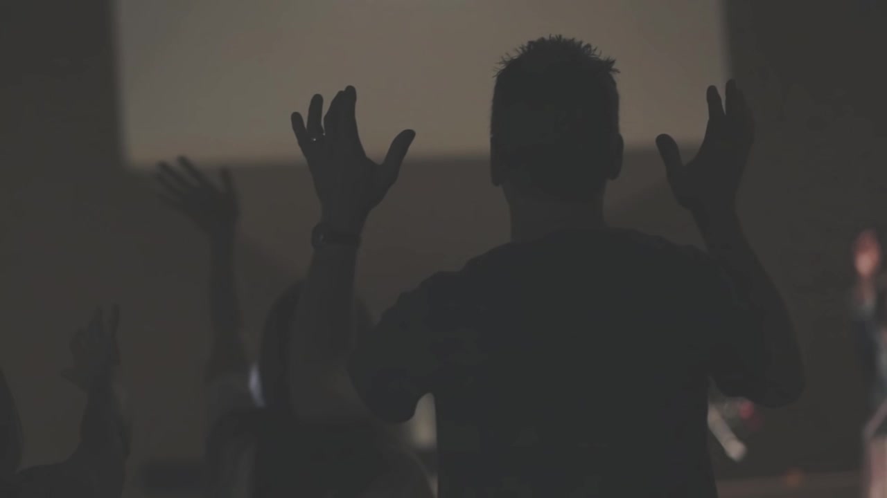 Persone con le mani alzate in silhouette durante una funzione religiosa