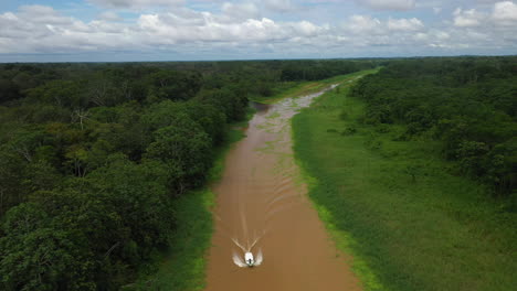 wide rising drone shot with a boat coming down the amazon river and the rainforest surrounding the river in peru