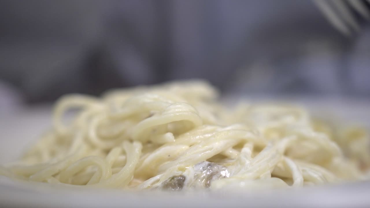 Un bambino mangia pasta alla panna in un ristorante. La mano del bambino tiene una forchetta. Primo piano sulla pasta