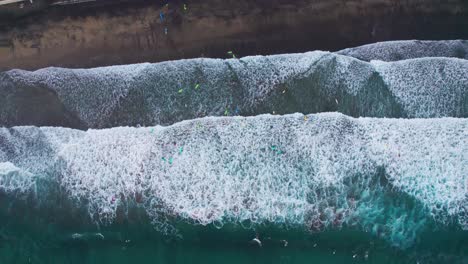 Top-down-aerial-view-of-surfers-riding-waves-at-Las-Canteras-Beach-,-Canary-Islands,-Europe