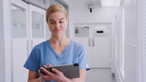 portrait of smiling female doctor wearing scrubs in hospital corridor using digital tablet