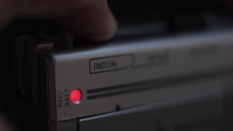 close-up of finger pressing record button of microcassette recorder and light coming on