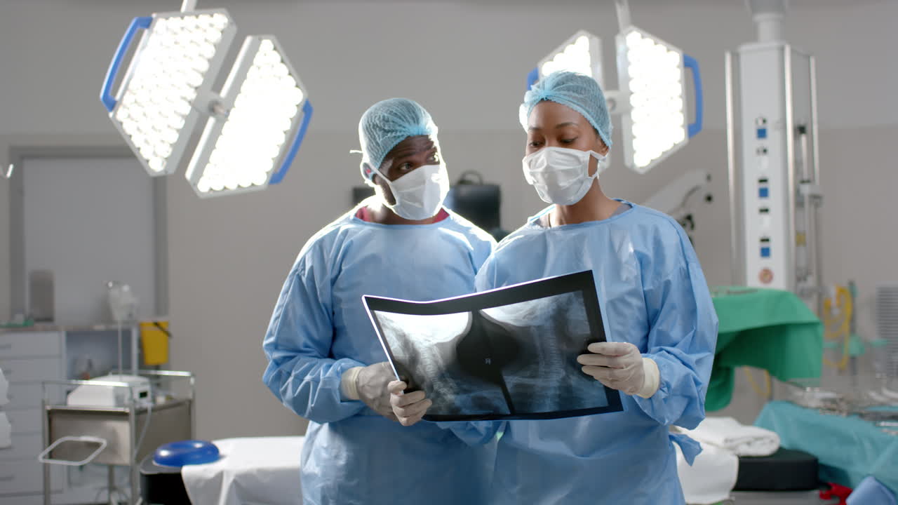 African american male and female surgeons looking at x-ray scans in operating theatre, slow motion