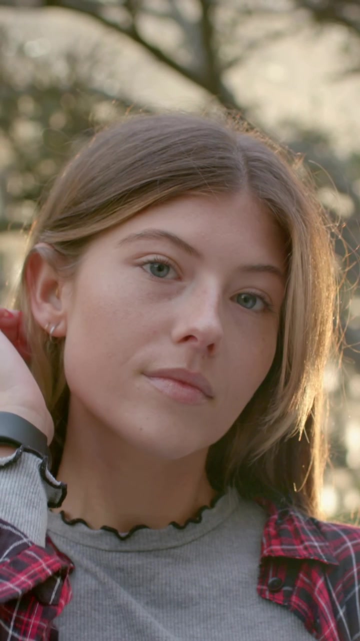 Video verticale: Donna inizia con la mano sulla tempia, si spazzola i capelli liberando il viso al parco, mostrando l'orologio.