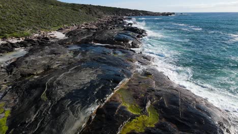 aerial view flying over rocks in empty beach with turquoise water