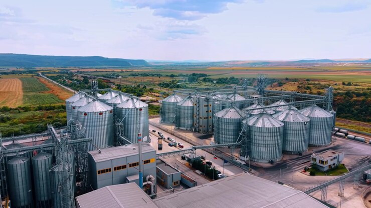 Varna, Bulgaria, 1 July 2026 : Large metallic grain silos at industrial storage facility. Aerial perspective shows tall silver tanks surrounded by green fields under a cloudy daytime sky.